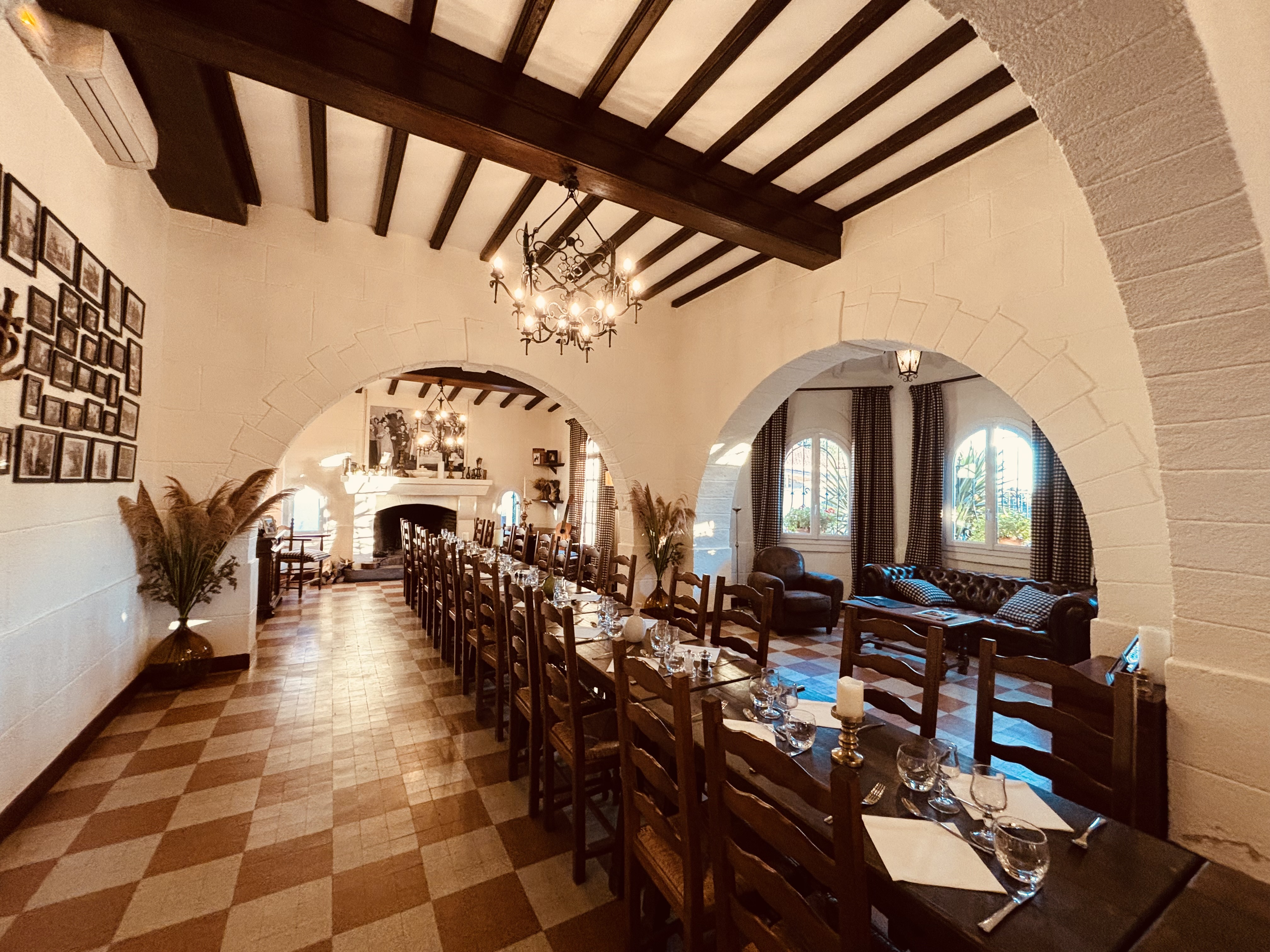 Salle de La Bergerie de Méjanes, tables dressées sous les poutres, arches blanches et cheminée. Photographie du partenaire.